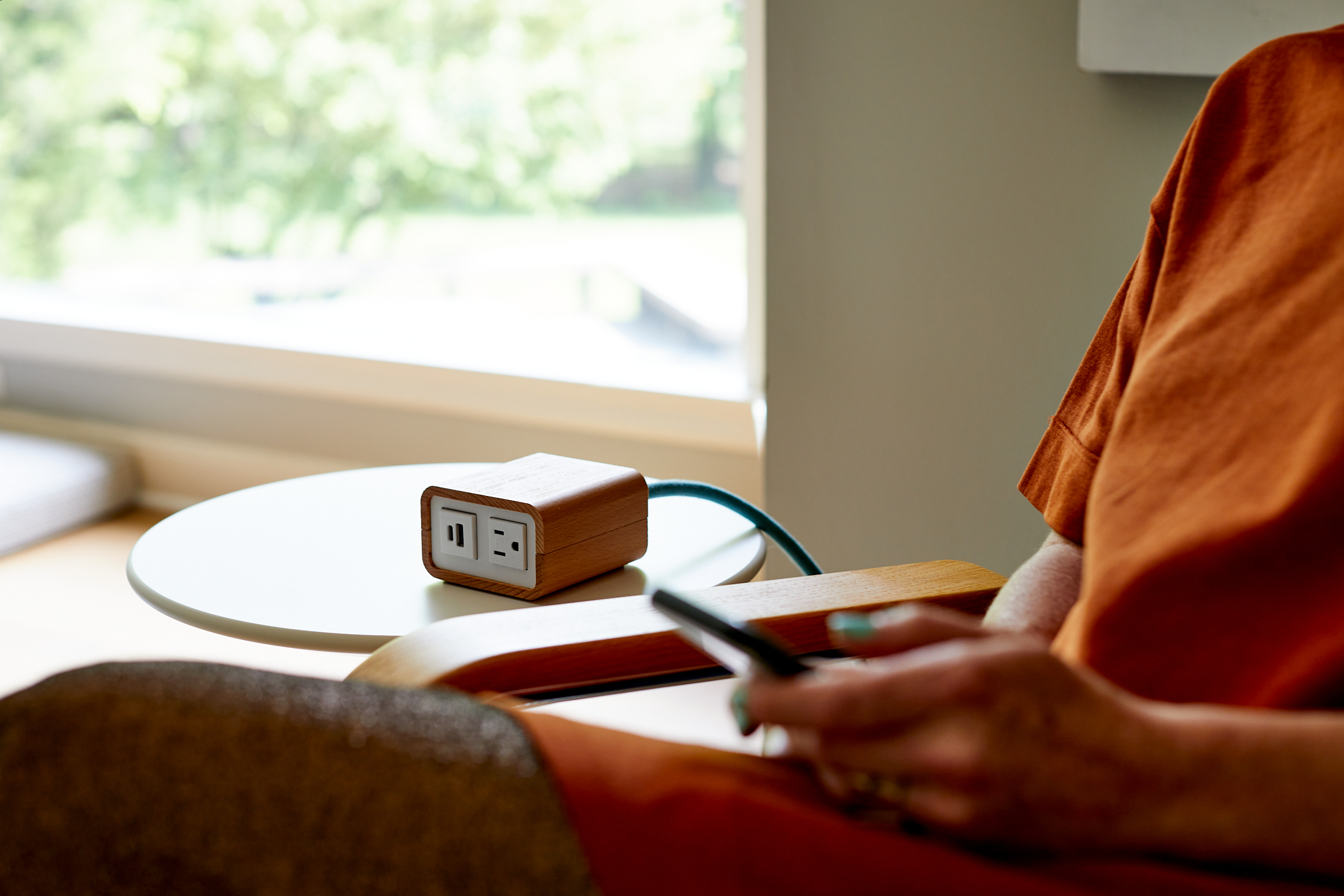 Close up of a person sitting holding their phone next to a side table with the Natural Wood Power on it.